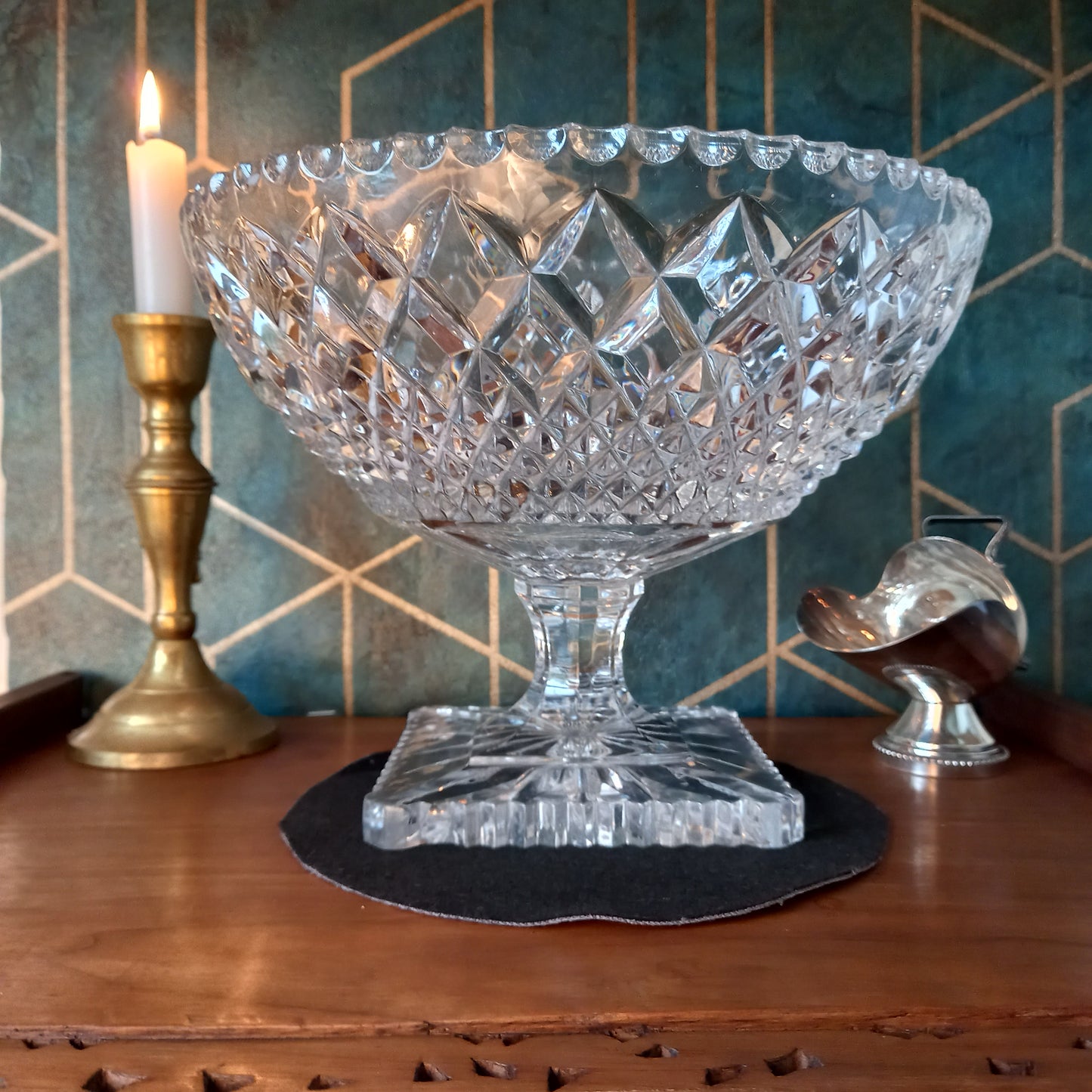 Elegant vintage cut crystal trifle bowl styled with candlelight and brass accents on a mahogany surface against a teal and gold Art Deco backdrop. The glass sparkles with intricate diamond cuts, evoking timeless luxury and craftsmanship.