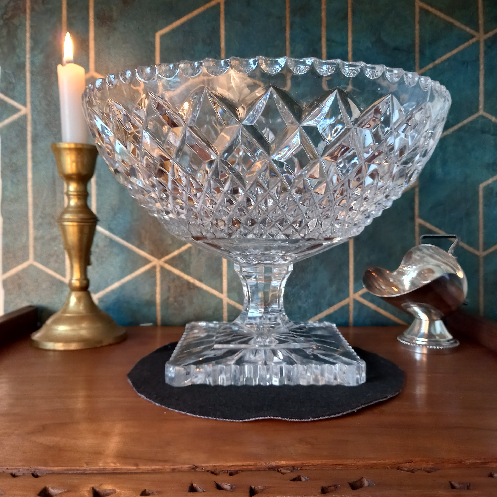 Elegant vintage cut crystal trifle bowl styled with candlelight and brass accents on a mahogany surface against a teal and gold Art Deco backdrop. The glass sparkles with intricate diamond cuts, evoking timeless luxury and craftsmanship.
