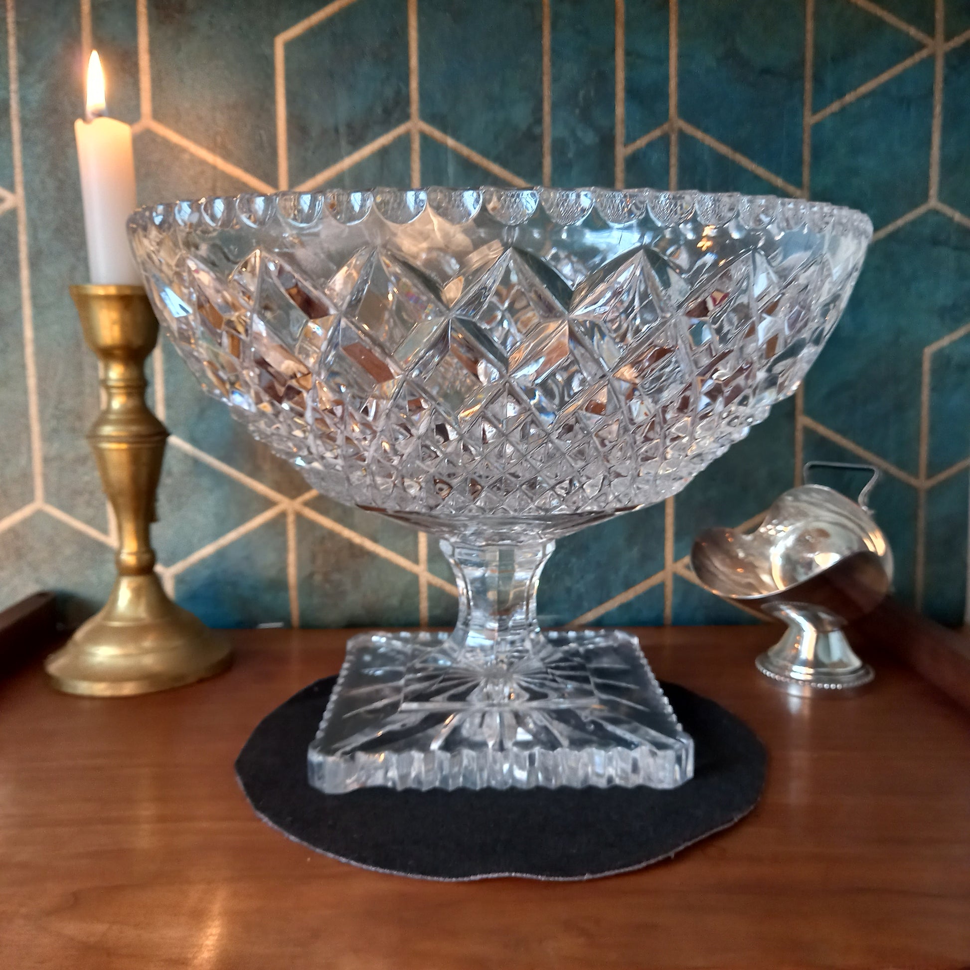Elegant vintage cut crystal trifle bowl styled with candlelight and brass accents on a mahogany surface against a teal and gold Art Deco backdrop. The glass sparkles with intricate diamond cuts, evoking timeless luxury and craftsmanship.