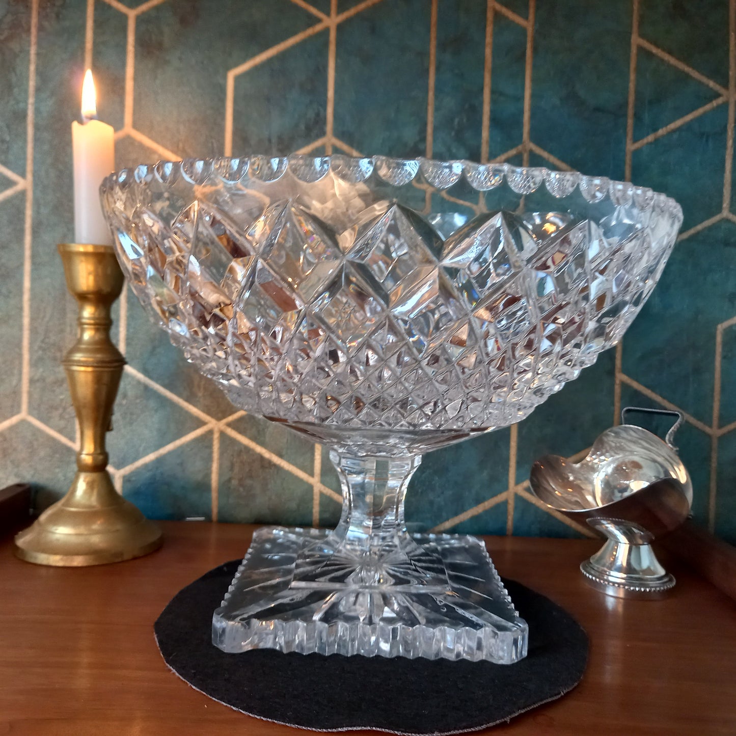 Elegant vintage cut crystal trifle bowl styled with candlelight and brass accents on a mahogany surface against a teal and gold Art Deco backdrop. The glass sparkles with intricate diamond cuts, evoking timeless luxury and craftsmanship.