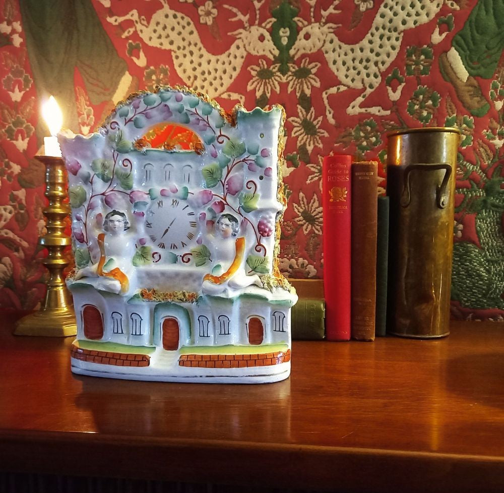 Victorian Staffordshire flatback clock group mantel ornament in glazed earthenware, circa 1850–1875, styled on dark wood library mantel with brass candlestick and antique books