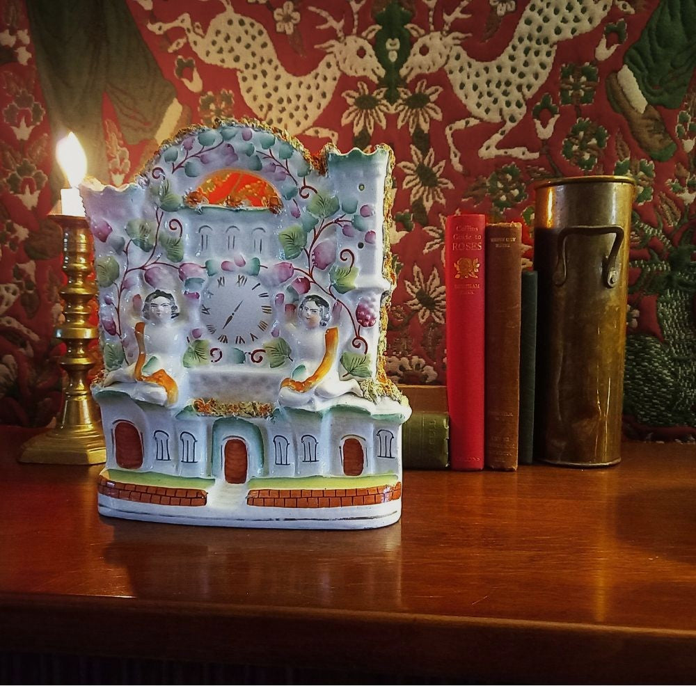 Victorian Staffordshire flatback clock group mantel ornament in glazed earthenware, circa 1850–1875, styled on dark wood library mantel with brass candlestick and antique books