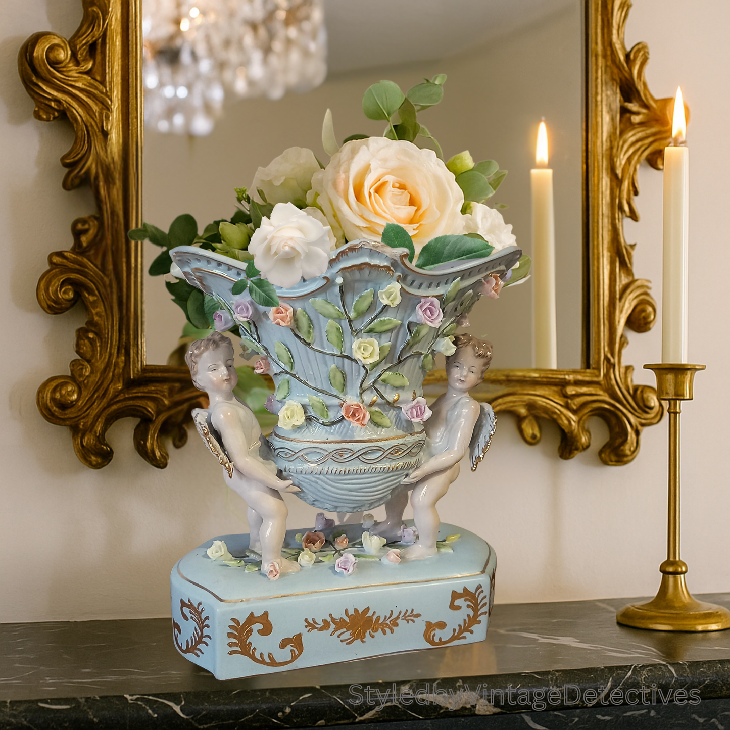 Capodimonte-style duck-egg blue vase with gilded cherubs and raised floral detail, styled on a marble mantle beneath a gilt mirror with candles and roses