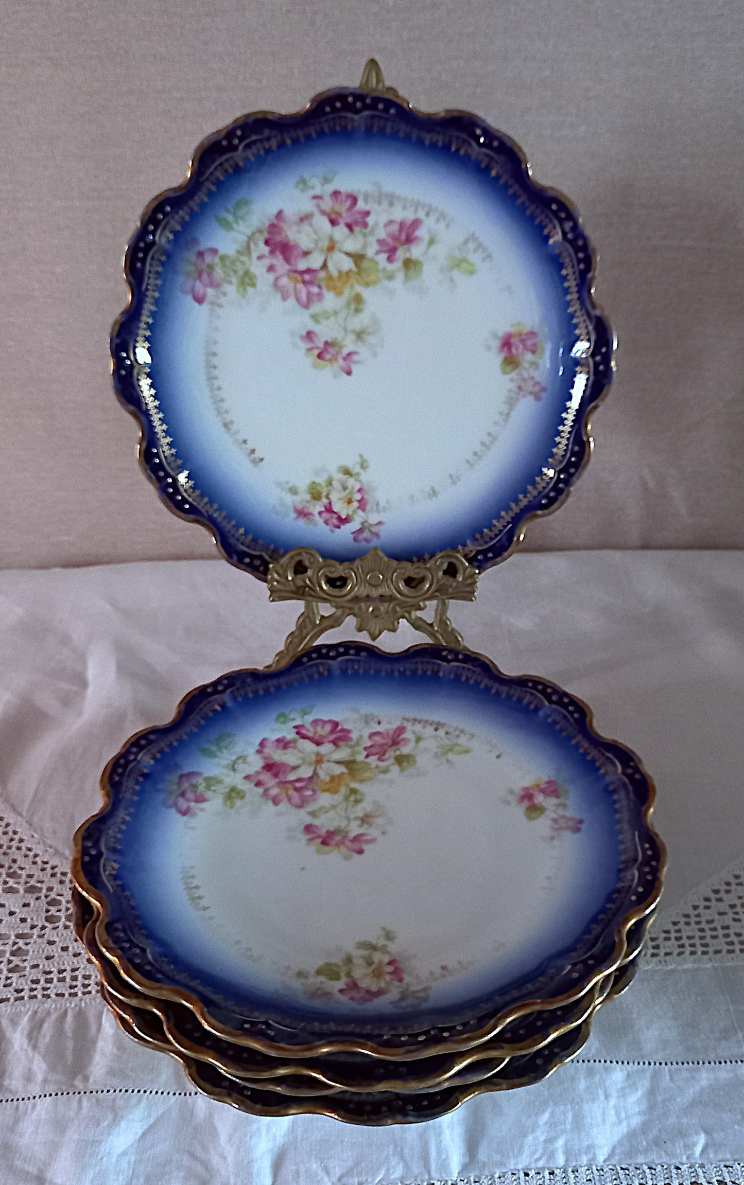 Stack of antique Limoges dessert plates with cobalt blue ombré rims, gold edging and floral pattern, displayed with one plate on an ornate brass stand.