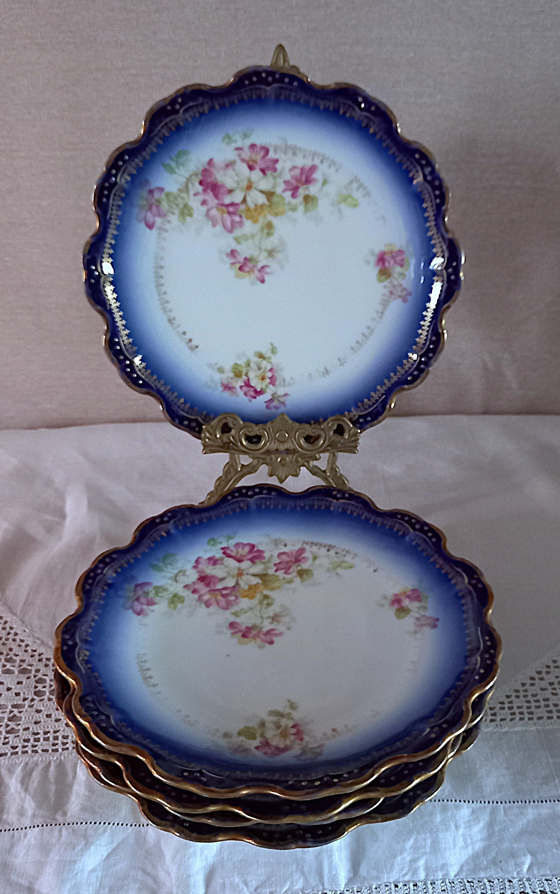 Stack of antique Limoges dessert plates with cobalt blue ombré rims, gold edging and floral pattern, displayed with one plate on an ornate brass stand.